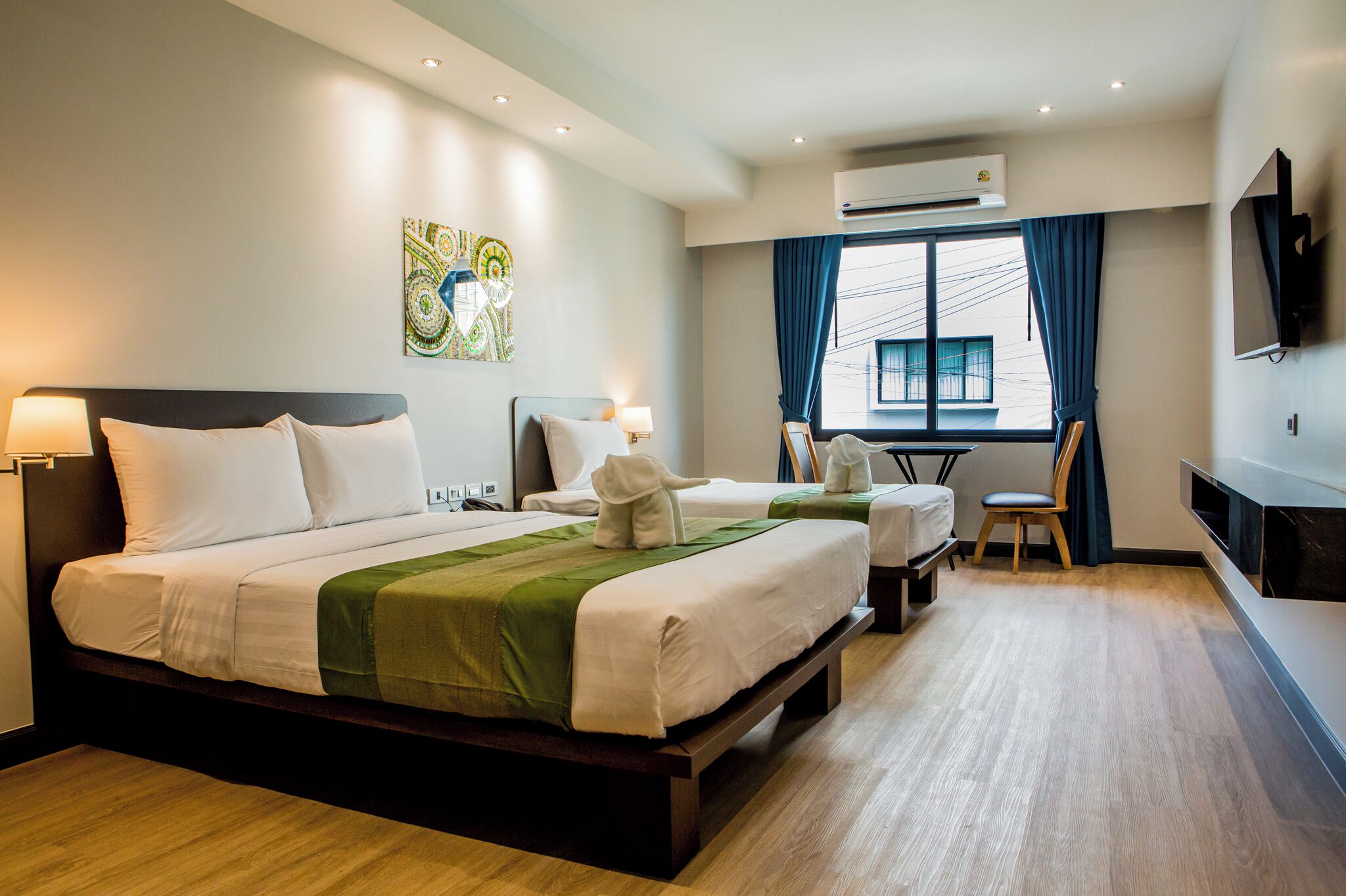 A hotel room with a large bed, a smaller bed, a desk, a chair, and a TV.