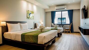 Quarto de hotel com uma cama grande, uma cama menor, uma escrivaninha, uma cadeira e uma televisão.