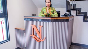 A reception desk with a large 'N' logo, a person standing behind it, and a staircase to the right. - Nouriva Place Bangkok (Bangkok)