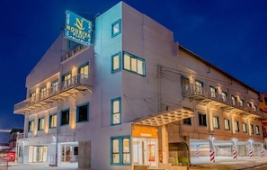 Um hotel com uma placa bem visível, várias varandas e entrada no nível da rua.