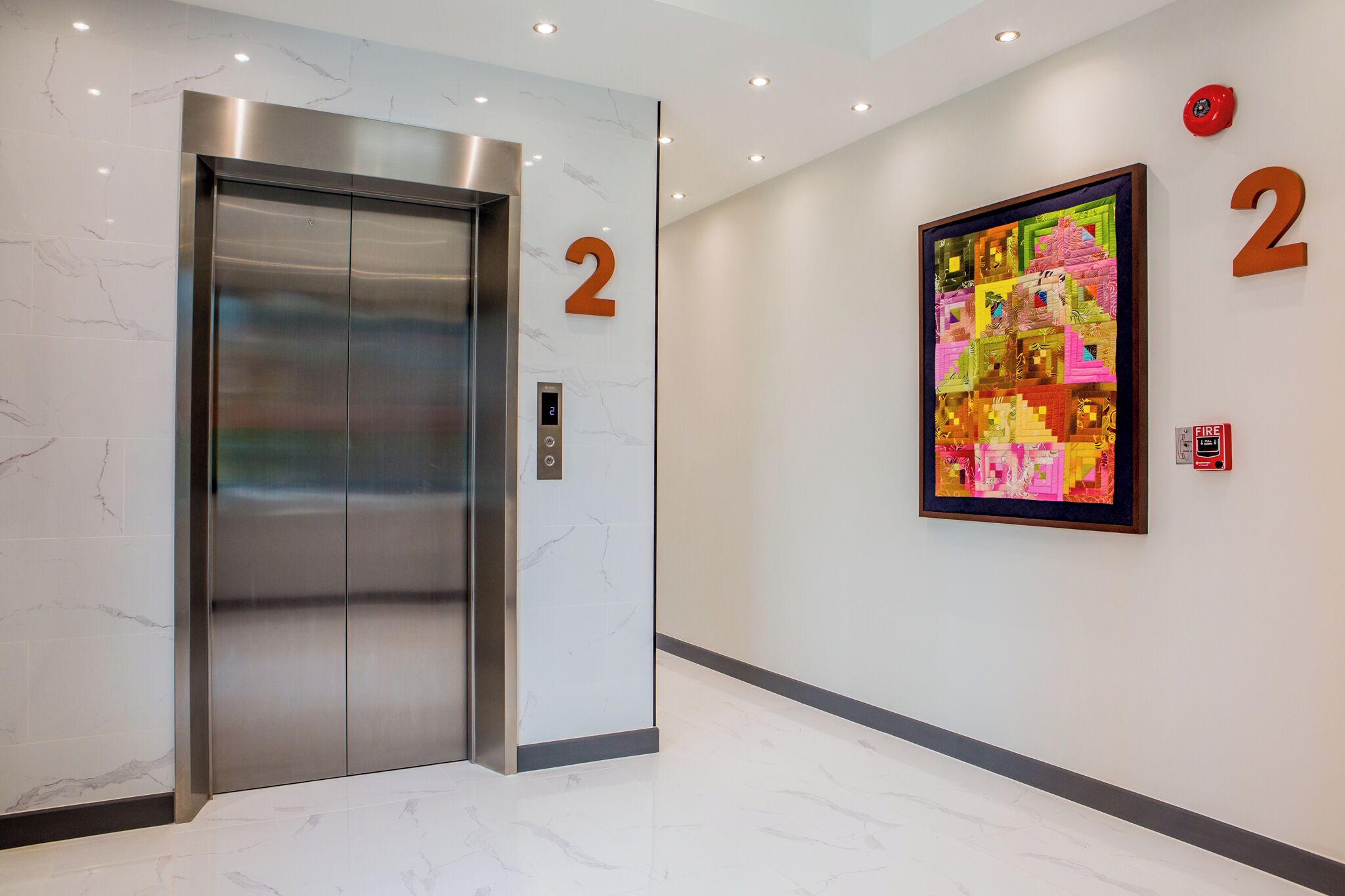 An elevator with a digital display, a number '2' sign, and a colorful artwork on the wall.