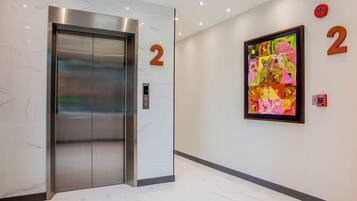An elevator with a digital display, a number '2' sign, and a colorful artwork on the wall.