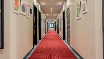 A hotel hallway with a red carpet, framed floral artwork on the walls, and doors leading to rooms.