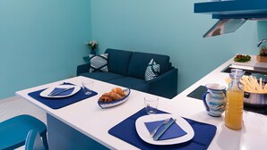 A modern kitchen with a white countertop, blue chairs, and a blue sofa.