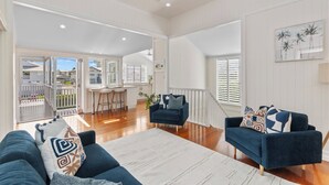 A spacious living room with a large sofa, a coffee table, and a dining area with bar stools. - Coastal Corner Luxury Queenslander on The Strand (North Ward)