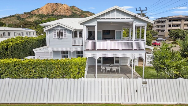 A two-story house with a balcony, a fenced yard, and a mountain in the background. - Coastal Corner Luxury Queenslander on The Strand (North Ward)