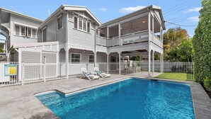 A two-story house with a swimming pool, a covered patio, and a fenced area with lounge chairs. - Coastal Corner Luxury Queenslander on The Strand (North Ward)