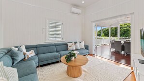 A modern living room with a sectional sofa, a round wooden coffee table, and a view of an outdoor patio area. - Coastal Corner Luxury Queenslander on The Strand (North Ward)