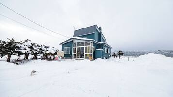 Una casa con techo inclinado, amplias ventanas y un paisaje cubierto de nieve.