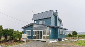 A two-story house with a large glass door entrance, a satellite dish, and a small outdoor area with a gravel path.