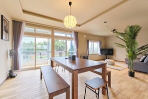 Un amplio espacio habitable con una mesa de madera para comer, bancos, un sofá, un televisor y un ventanal con vistas.