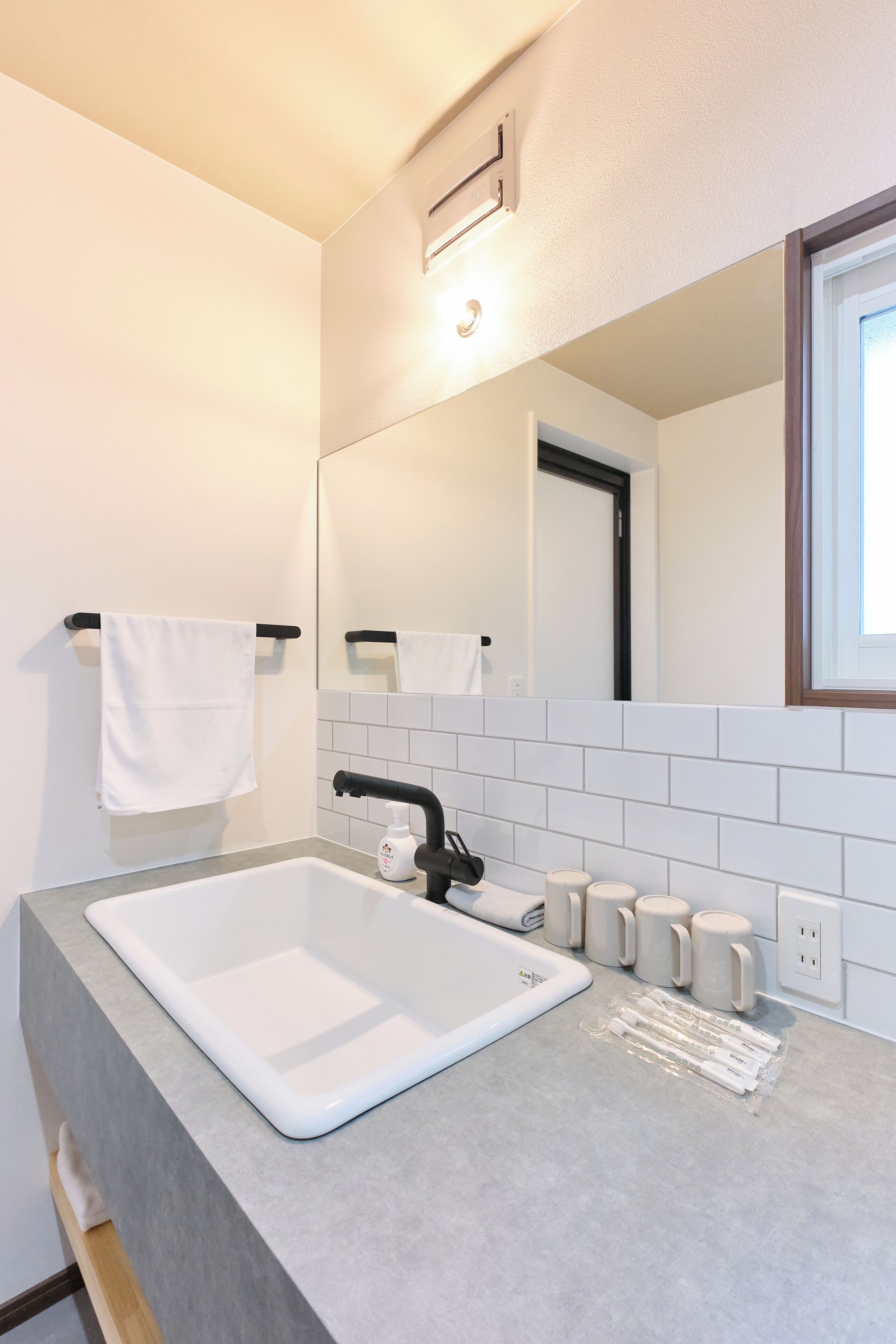 A bathroom with a white sink, black faucet, and a mirror above it. There are white tiles on the wall and a window with a wooden frame.