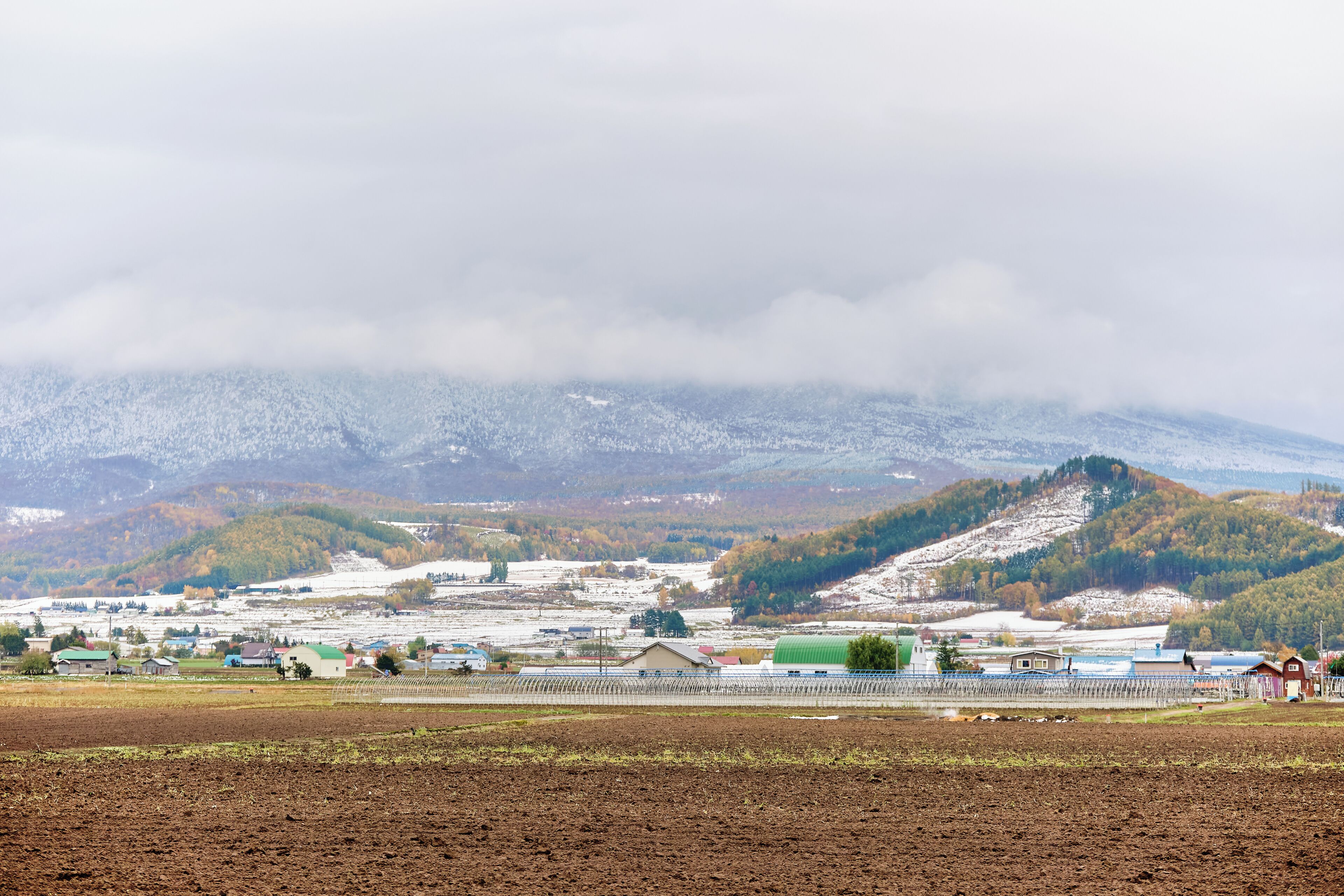 A rural landscape with fields, a few buildings, and a mountain in the background.