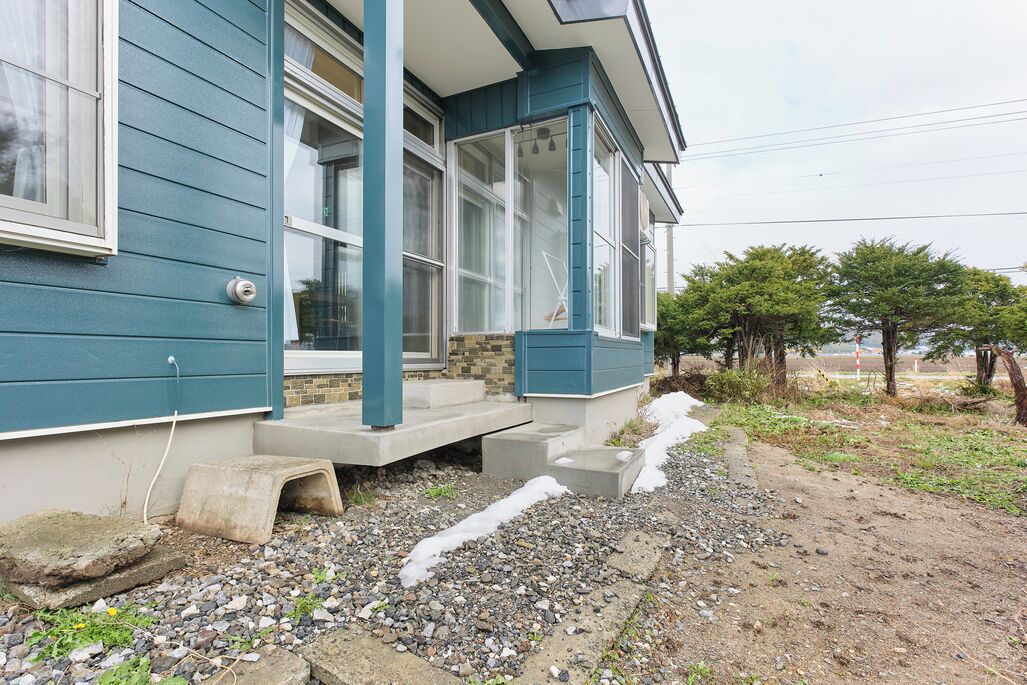 A house with a porch, a stone foundation, and a gravel driveway.