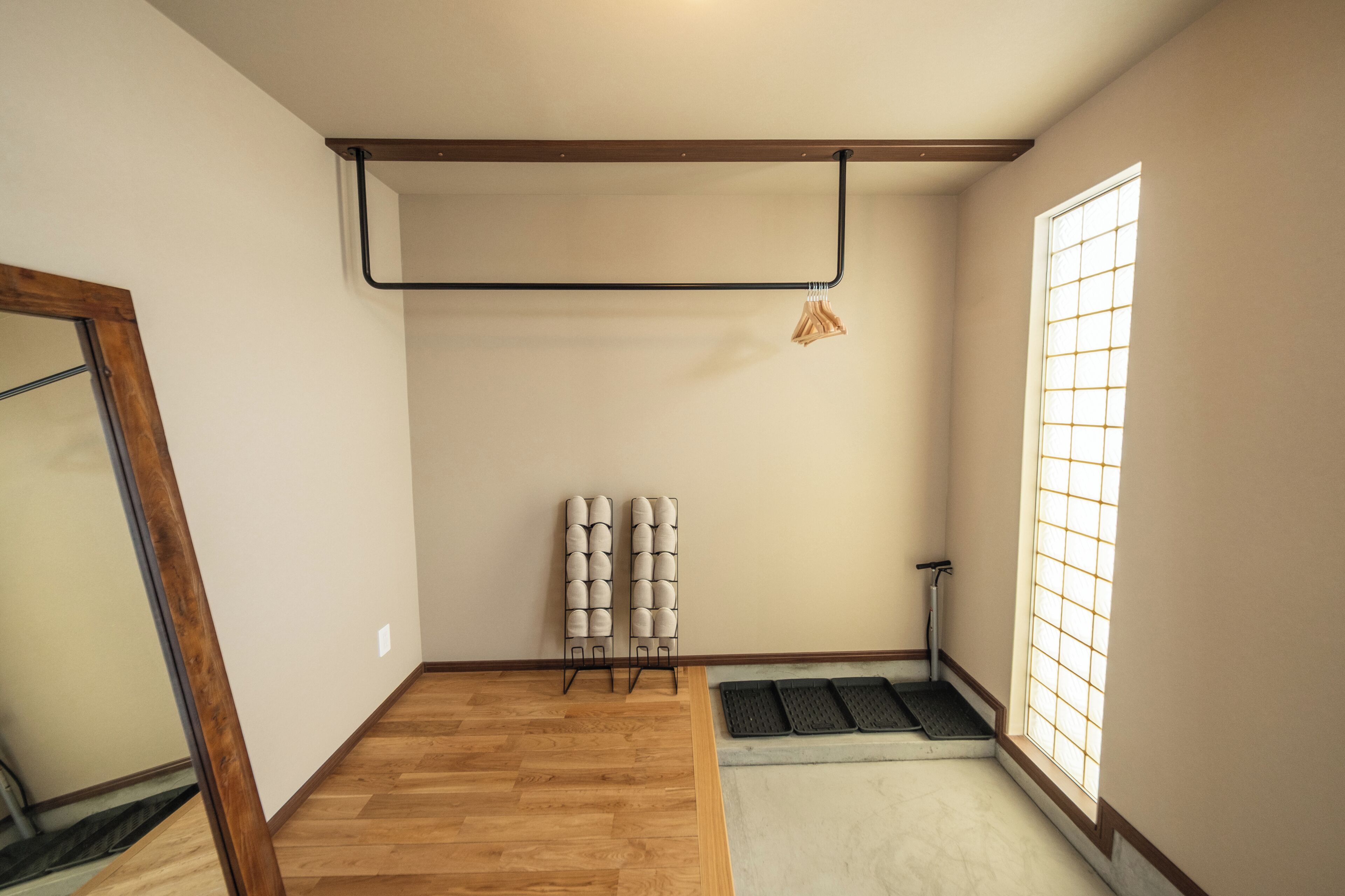Una habitación con piso de madera, una ventana con diseño de cuadrícula, un tapete negro en la entrada y un perchero en la pared con objetos doblados.