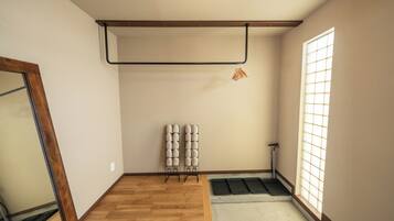 Una habitación con piso de madera, una ventana con diseño de cuadrícula, un tapete negro en la entrada y un perchero en la pared con objetos doblados.