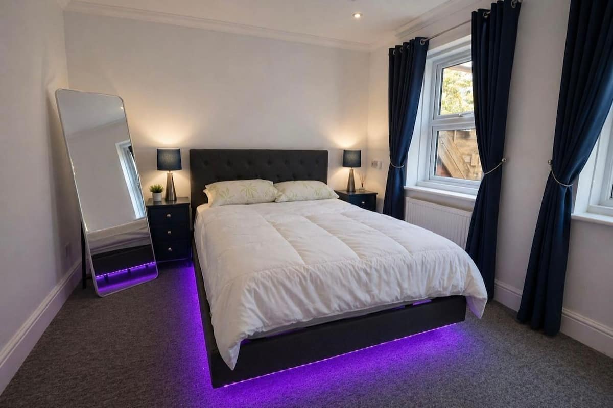 Un dormitorio moderno con una cama grande, lámparas de noche, un espejo y una ventana con cortinas.