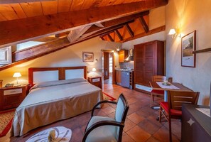 Une chambre avec un grand lit, un bureau, une chaise et un coin cuisine.