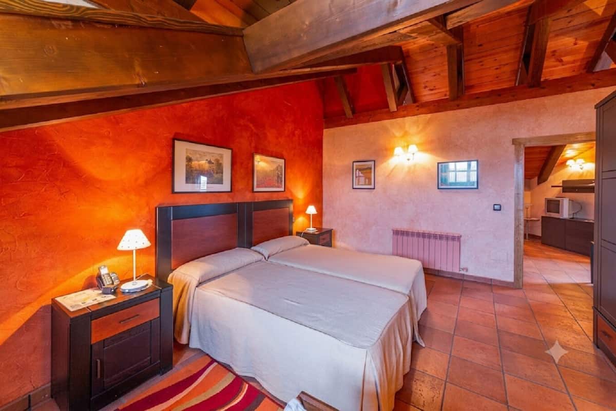 Un dormitorio con una cama grande, dos mesitas de noche con lámparas, un radiador y vista a la cocina.