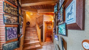 A hallway with a staircase, framed artwork, and a small toy house on the floor.