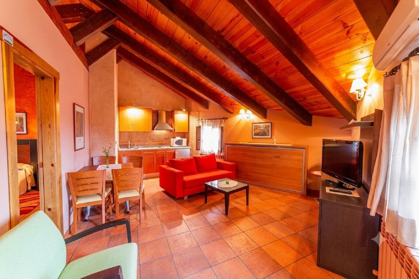 Una sala de estar acogedora con un sofá rojo, muebles de madera, un televisor y una cocina al fondo.