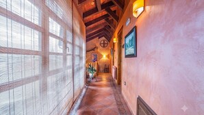 A corridor with wooden beams, a tiled floor, and wall-mounted lights.