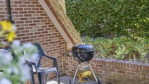 A barbecue grill on a patio with a brick wall and a hedge in the background.