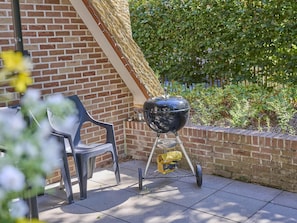 Una parrilla para barbacoa en un patio con un muro de ladrillo y un seto al fondo.