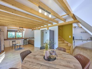 Un interior moderno con una mesa de comedor de madera, sillas, una cocina y una escalera.