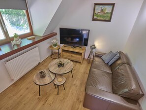 A cozy living room with a brown leather sofa, a wooden coffee table, a TV, and a small side table with a plant.