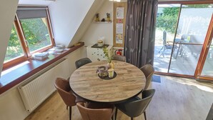 A dining area with a round wooden table, leather chairs, a vase with flowers, and a view of the outdoors through large windows.