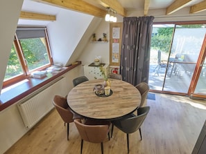 Un comedor con una mesa redonda de madera, sillas de cuero, un jarrón con flores y vistas al exterior a través de amplias ventanas.