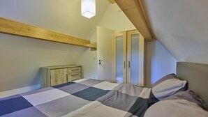 A bedroom with a checkered bedspread, wooden ceiling beams, a wardrobe, and a door with frosted glass panels.