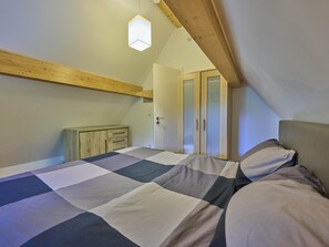 Un dormitorio con colcha a cuadros, vigas de techo de madera, un armario y una puerta con paneles de vidrio esmerilado.