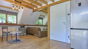 A modern kitchen with a built-in refrigerator, wooden beams, a dining area with a table and chairs, and a large window providing natural light.