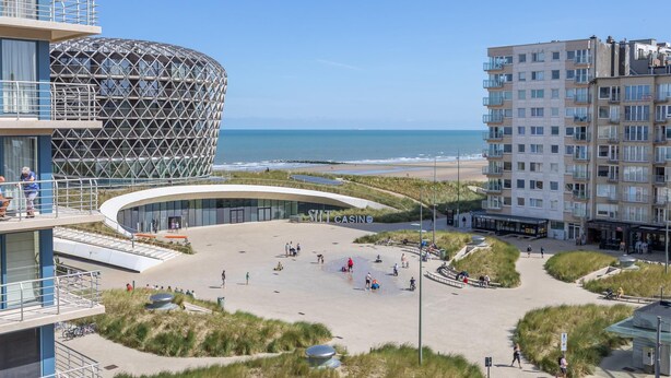 Ein modernes Gebäude mit einer einzigartigen, kugelförmigen Struktur, einer Promenade mit Menschen und einem Strand im Hintergrund.