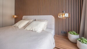Ein modernes Schlafzimmer mit einer Wand aus Holzlamellen, einem Bett mit zwei Kissen, zwei Pendelleuchten und zwei Topfpflanzen.