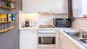 Une cuisine compacte avec des meubles blancs, un four à micro-ondes, une bouilloire et un grille-pain.