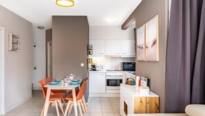 Une cuisine moderne avec des meubles blancs, une table à manger avec des chaises orange et un canapé blanc.