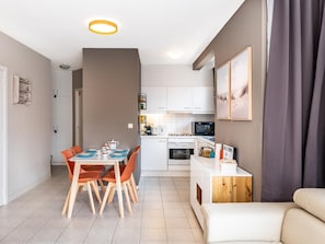 Eine moderne Küche mit weißen Schränken, einem Esstisch mit orangefarbenen Stühlen und einem weißen Sofa.