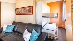 Una habitación con un sofá de cuero negro, una litera, un tapiz enmarcado y una puerta que da a otra habitación.
