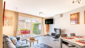 Una sala de estar moderna con un sofá, una mesa de comedor para dos personas y un televisor montado en la pared.