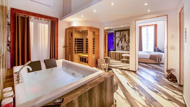 Ein modernes Hotelzimmer mit einer großen Badewanne, einem begehbaren Kleiderschrank, einem separaten Badezimmer inklusive Badewanne und Blick auf die Stadt.
