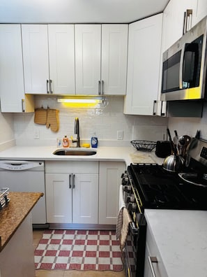 A kitchen with white cabinets, a stainless steel stove, a microwave, and a sink.