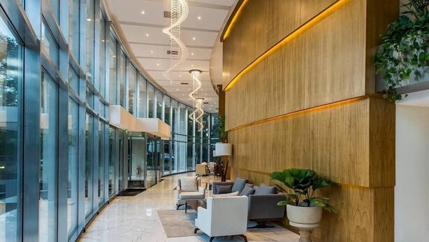 A modern lobby with a curved glass wall, a wooden reception desk, seating area, and a chandelier. - Corporate Stays The Tower (Asunción)