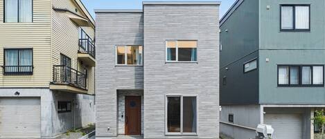 A modern two-story building with a central entrance, a garage, and a small garden area.
