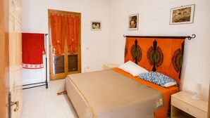 Quarto com cama, mesa de cabeceira, janela com cortinas e porta.
