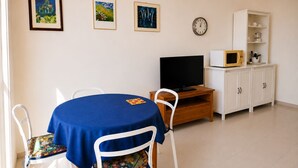 Uma sala de jantar com uma mesa redonda, cadeiras, televisão, relógio e um armário com prateleiras.