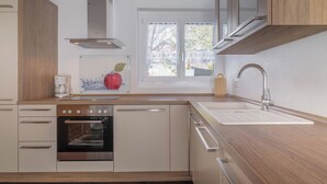 Moderni keittiö, jossa on sisäänrakennettu uuni, pesuallas ja puiset kaapit.