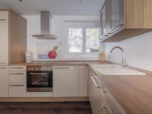 A modern kitchen with a built-in oven, a sink, and wooden cabinetry. - Alpen Leukerbad # 2-bed apartment, Dusche, WC by Interhome (Leukerbad)